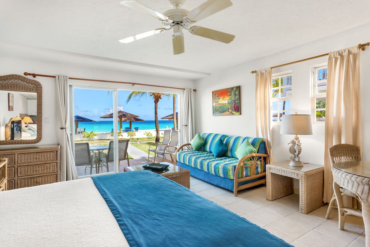 Een hotelkamer met een bed, een slaapbank, een bureau en uitzicht op het strand.