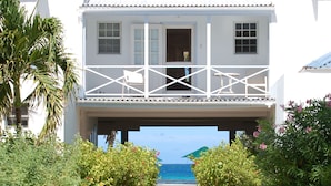 A white building with a balcony overlooking a swimming pool and the ocean.