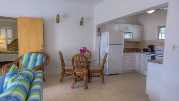 A compact kitchen with white cabinets, a refrigerator, and a microwave. There is a dining table with chairs and a small vase with flowers.
