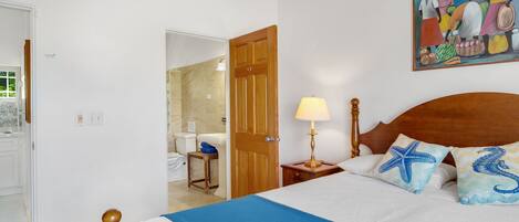 Habitación de hotel con cama, mesita de noche con lámpara, puerta de madera y un cuadro en la pared.