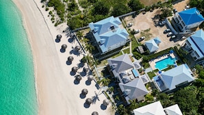 An aerial view of a coastal resort with multiple buildings, a swimming pool, and beach umbrellas.