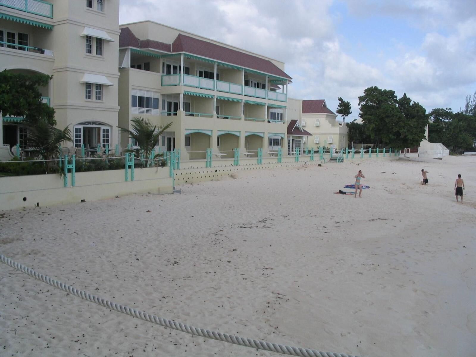 Un hôtel situé en bord de mer, avec une structure à deux étages, des balcons et une plage de sable.