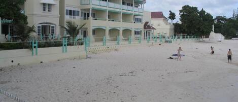 Un hotel frente a la playa con una estructura de dos pisos, balcones y una zona de arena.
