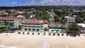 Un hotel frente a la playa con varias construcciones, una piscina y sombrillas.