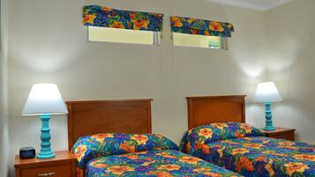 A hotel room with two beds, each with a floral bedspread, wooden headboards, and bedside lamps. There are two wall-mounted mirrors above the beds.