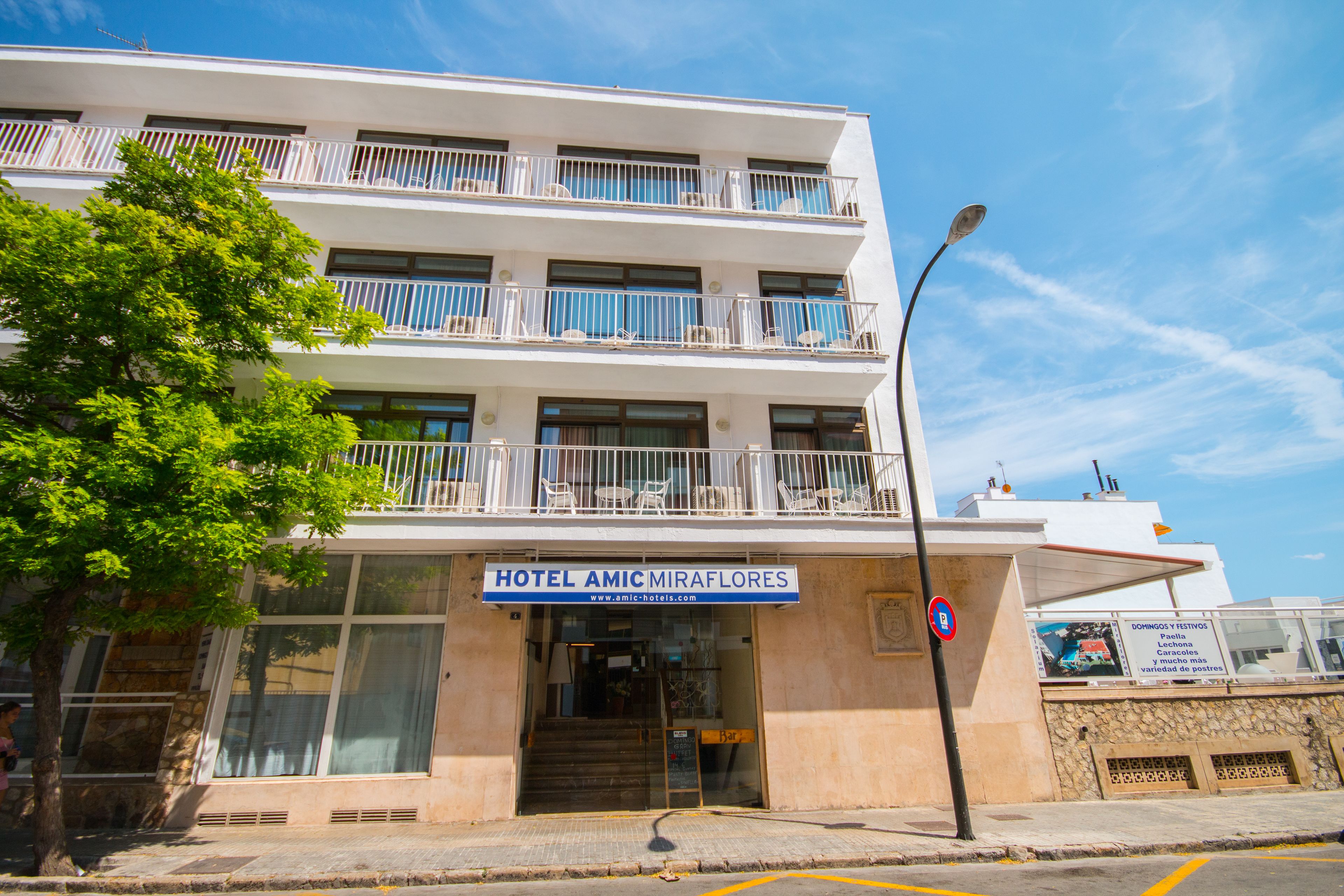 Um hotel com vários andares, varandas, uma entrada visível e uma placa indicando que é um hotel.