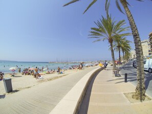 Une plage bordée de palmiers, une promenade et, au loin, un port de plaisance.