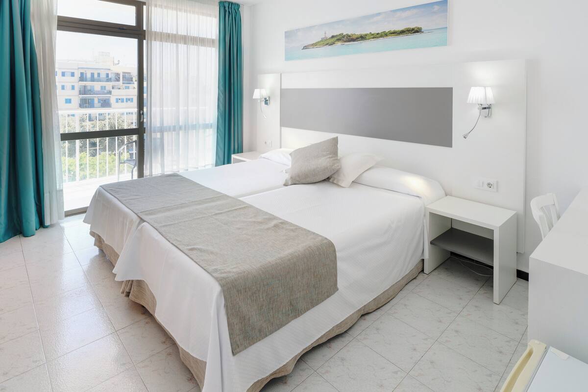 Quarto de hotel com uma cama grande, mesa de cabeceira e janela com cortinas.
