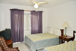A bedroom with two beds, a ceiling fan, a lamp, and a chair. - Waterway Condos (Nassau)
