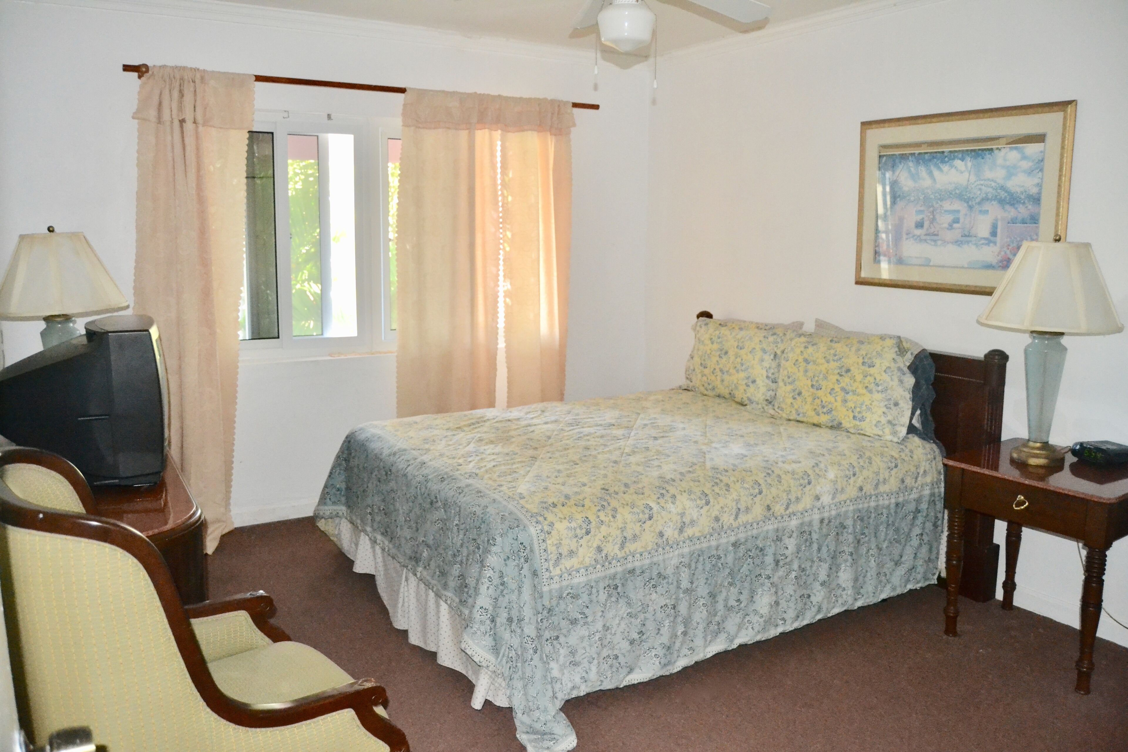A bedroom with a bed, two bedside tables with lamps, a chair, a television, and a window with curtains.