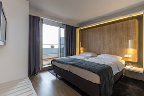 A modern hotel room with a large bed, a bedside table with a lamp, a wooden accent wall, and a view of the outdoors. - M Hotel Ljubljana (Ljubljana)