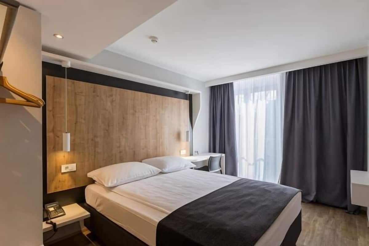 A hotel room with a large bed, bedside tables, a desk, and a window with curtains.