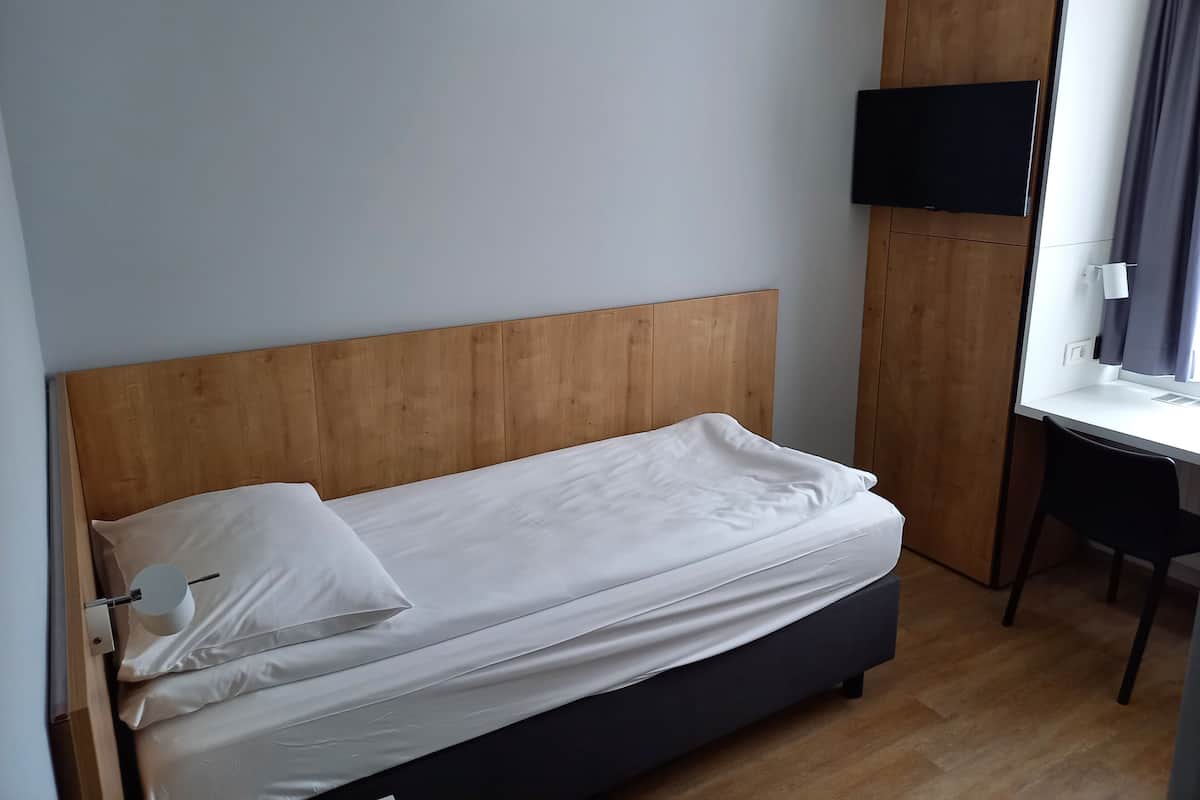 A single bed with a wooden headboard, a TV mounted on the wall, and a desk with a chair.