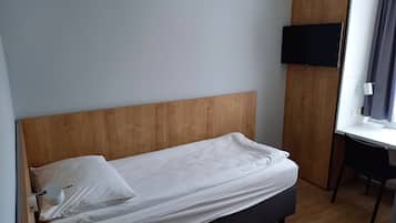 Una cama individual con cabecera de madera, un televisor montado en la pared y un escritorio con una silla.