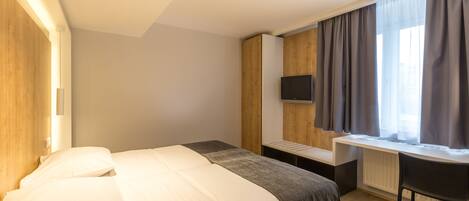 A modern hotel room with a large bed, a desk, and a TV.