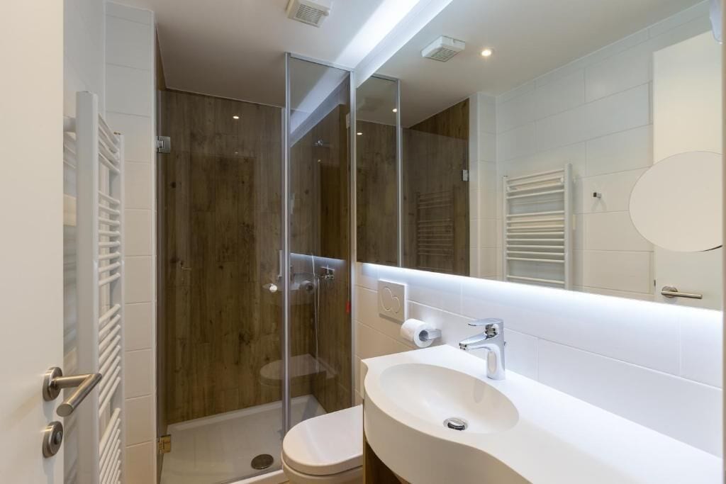 A modern bathroom with a glass shower enclosure, a white sink, and a large mirror.