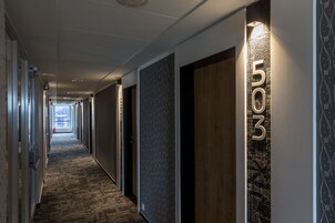 A modern hotel corridor with a carpeted floor, numbered doors, and a view into the distance.
