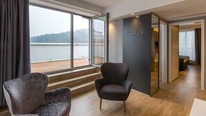 Una habitación moderna con un ventanal grande, un sillón oscuro y suelo de madera.