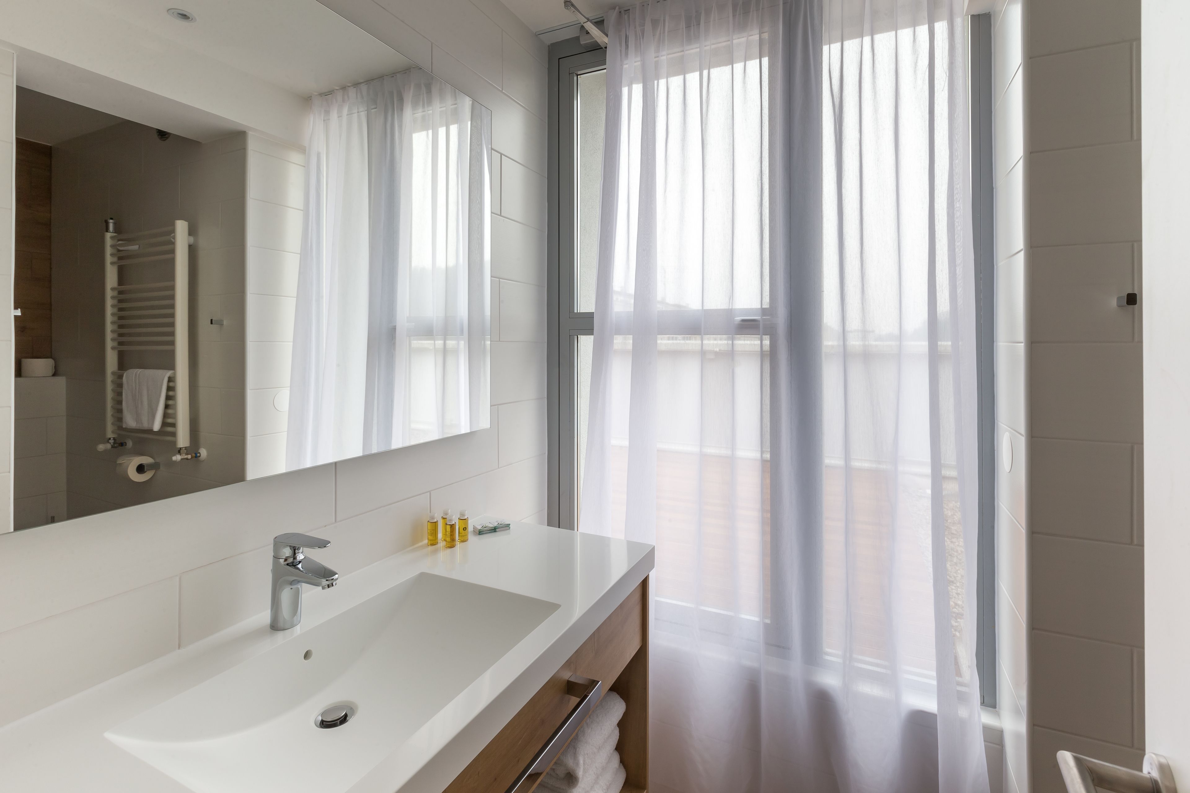 A modern bathroom with a large mirror, white sink, and a towel rack.