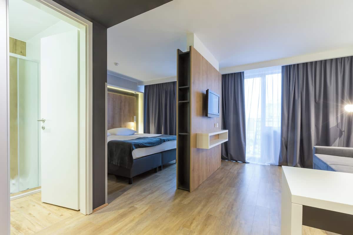 A modern hotel room with a bed, a TV, a desk, and a view of the outdoors.