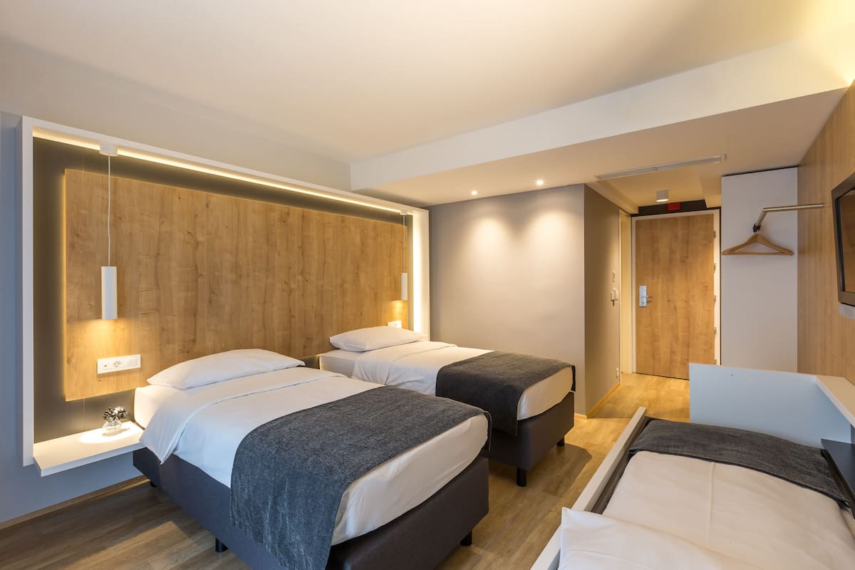 A modern hotel room with two beds, a wooden headboard, a bedside table, and a hanging light fixture.
