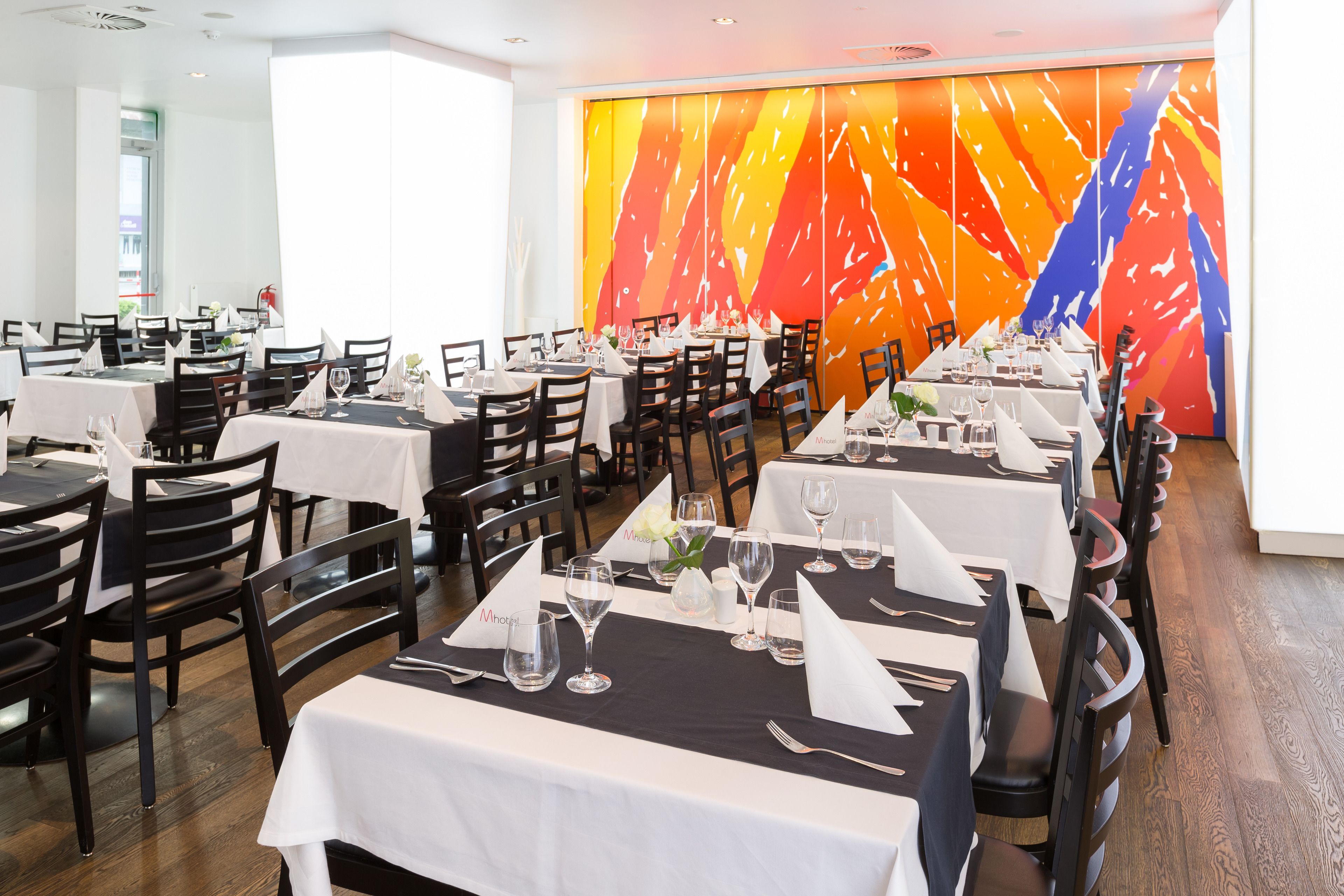 A restaurant with multiple tables set for dining, featuring white tablecloths and black chairs.