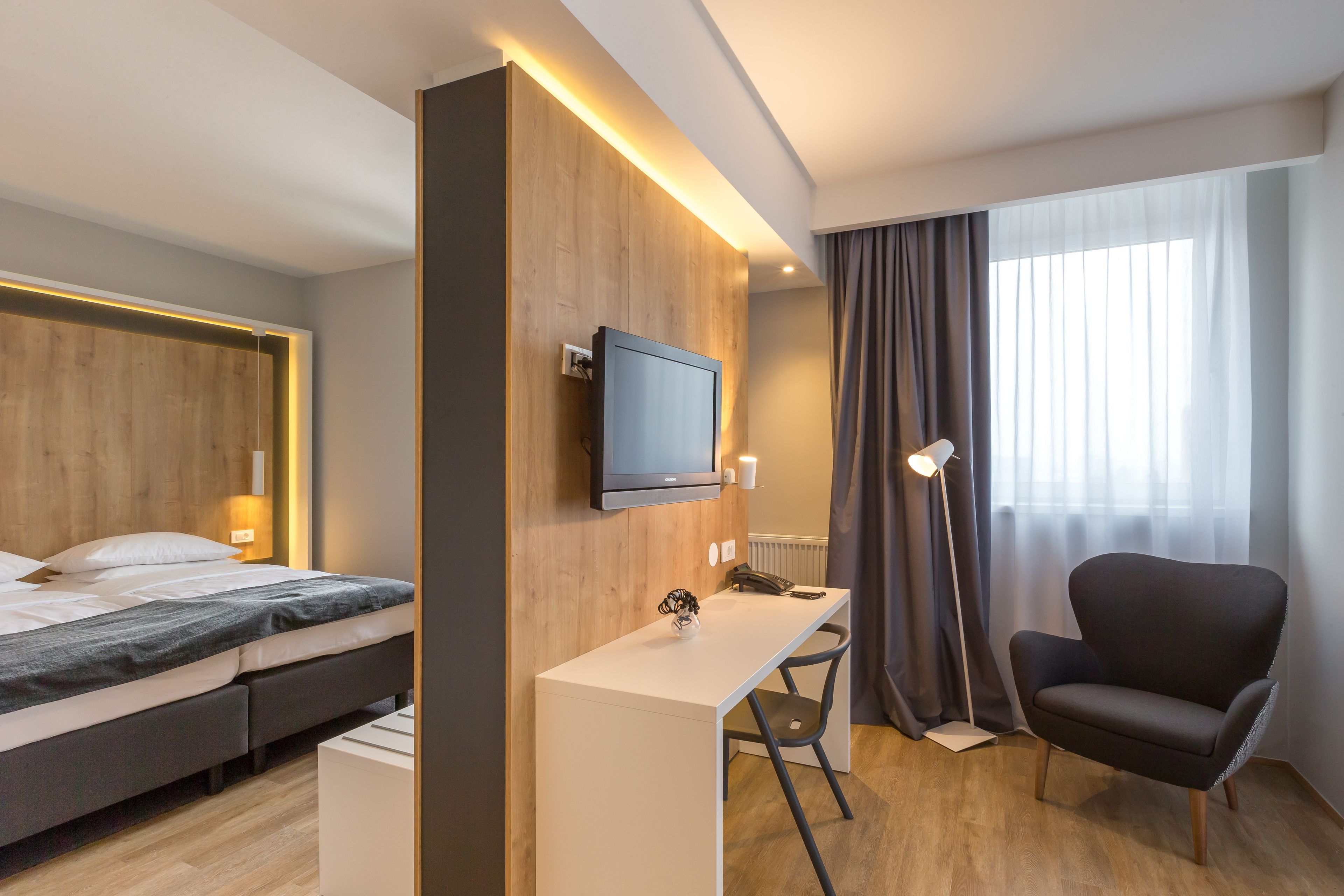 Habitación de hotel con cama, escritorio, silla, televisor y ventana con cortinas.