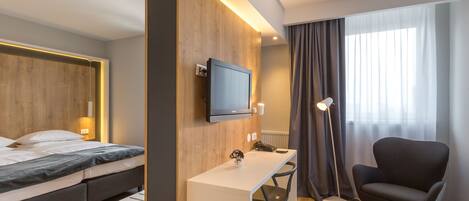 Habitación de hotel con cama, escritorio, silla, televisor y ventana con cortinas.