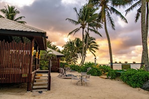 A beachside bungalow with a wooden deck, lounge chairs, and a table.