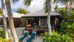 A beachside resort with lounge chairs, a covered seating area, and palm trees.