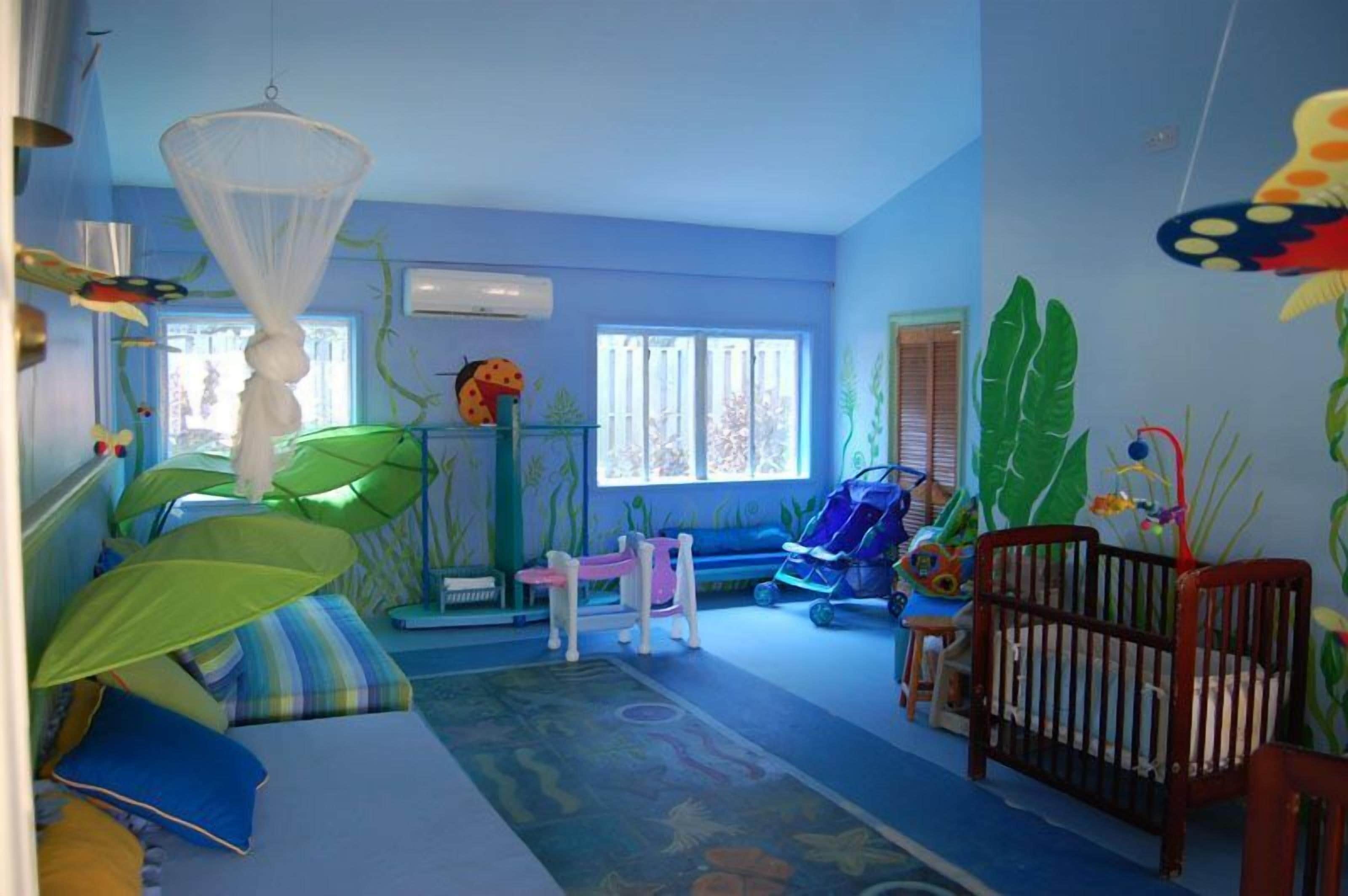 Une pièce avec un mur bleu, un lit doté d’un ciel de lit vert, un berceau et un espace de jeux avec un toboggan.