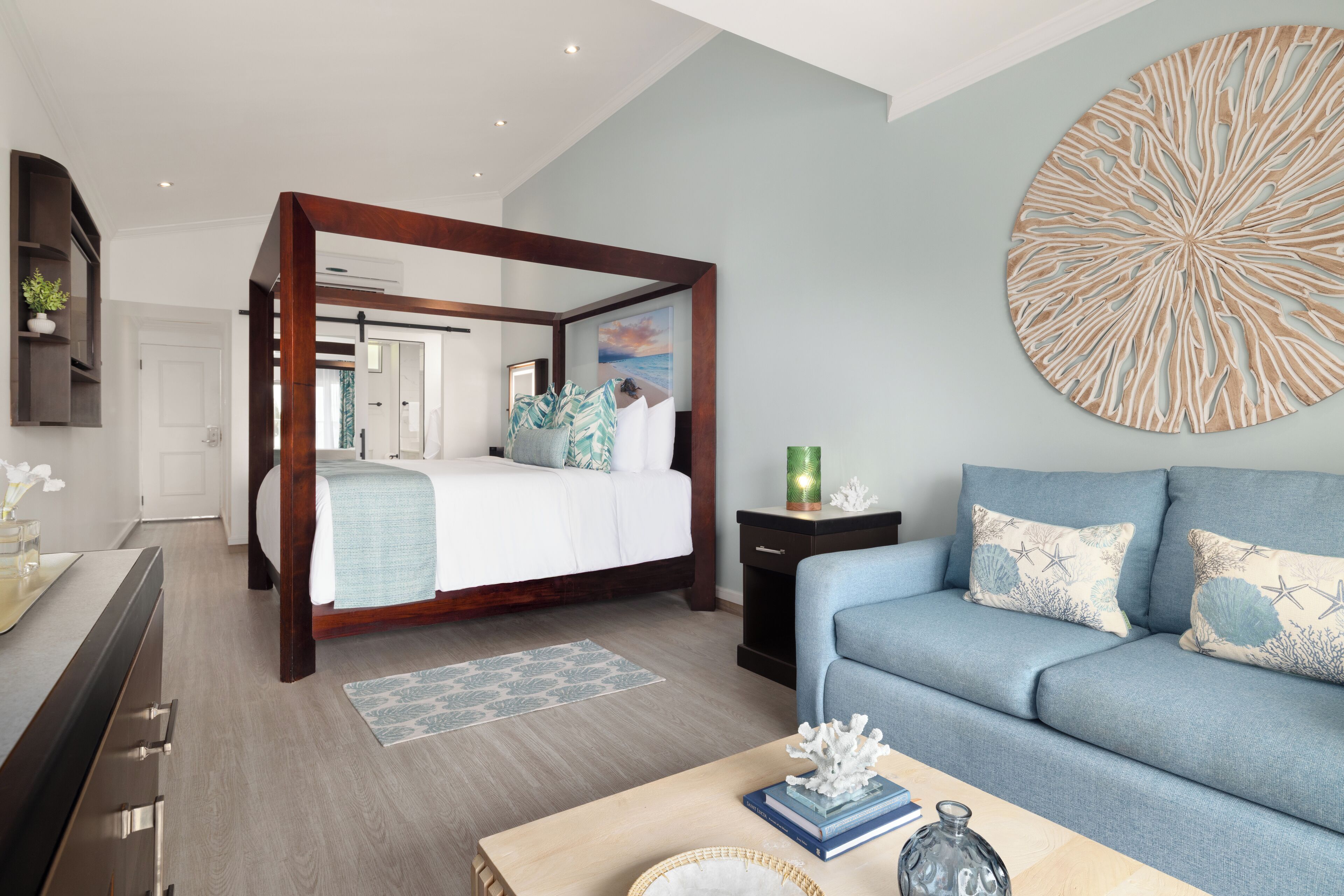 A modern bedroom with a four-poster bed, a blue sofa, and a decorative wall piece.