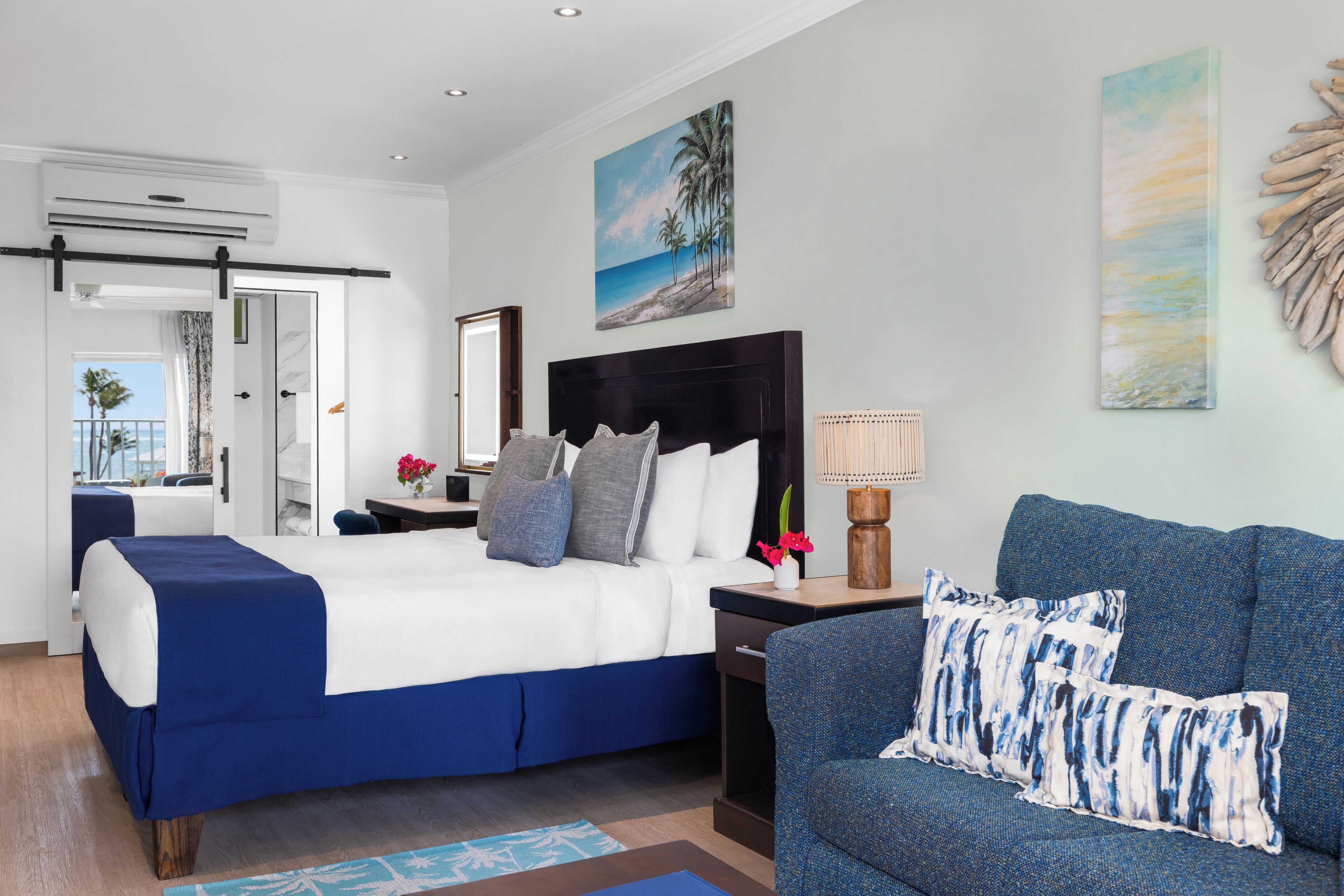 A hotel room with a bed, a sofa, a desk, and a painting of a beach scene.