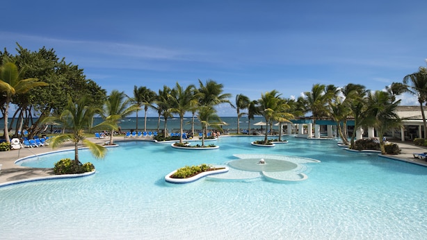 Une piscine de complexe hôtelier bordée de palmiers et dotée de chaises longues bleues.