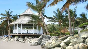 Relax in a serene coastal gazebo surrounded by palm trees and large rocks.