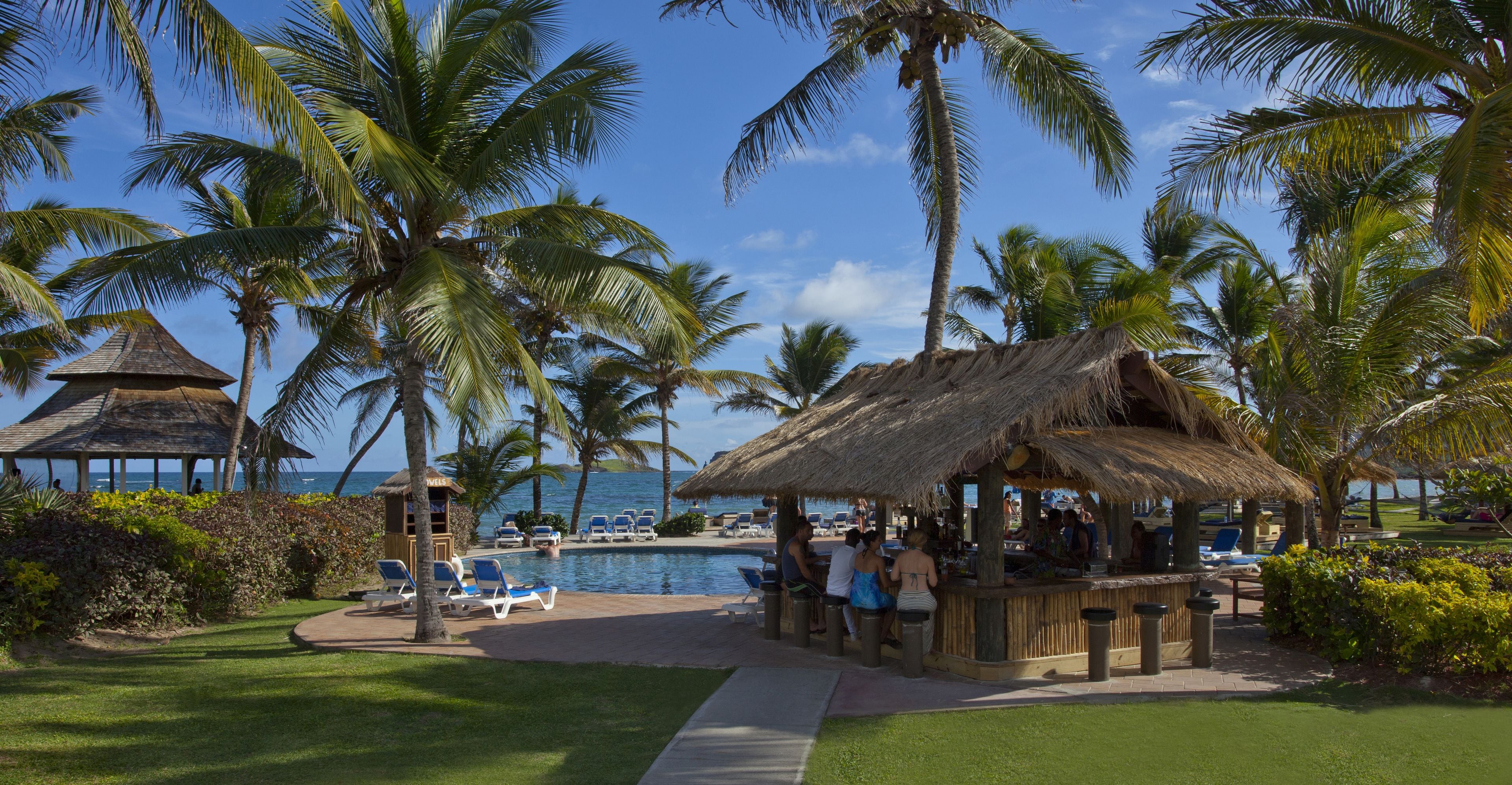 A poolside area with lounge chairs, a bar, and palm trees.