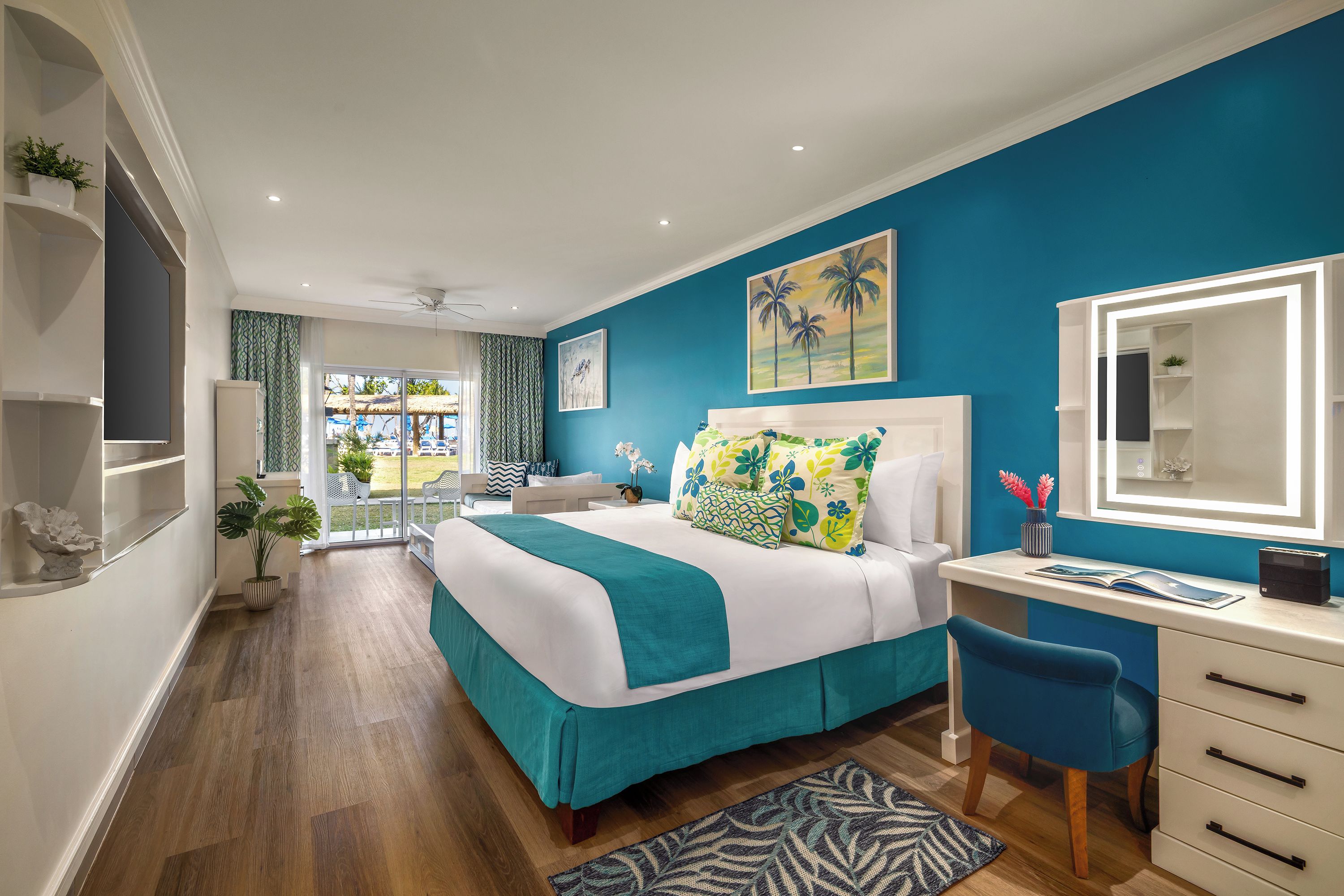 A modern bedroom with a large bed, a desk, and a chair. There is a balcony with a view of the outside.
