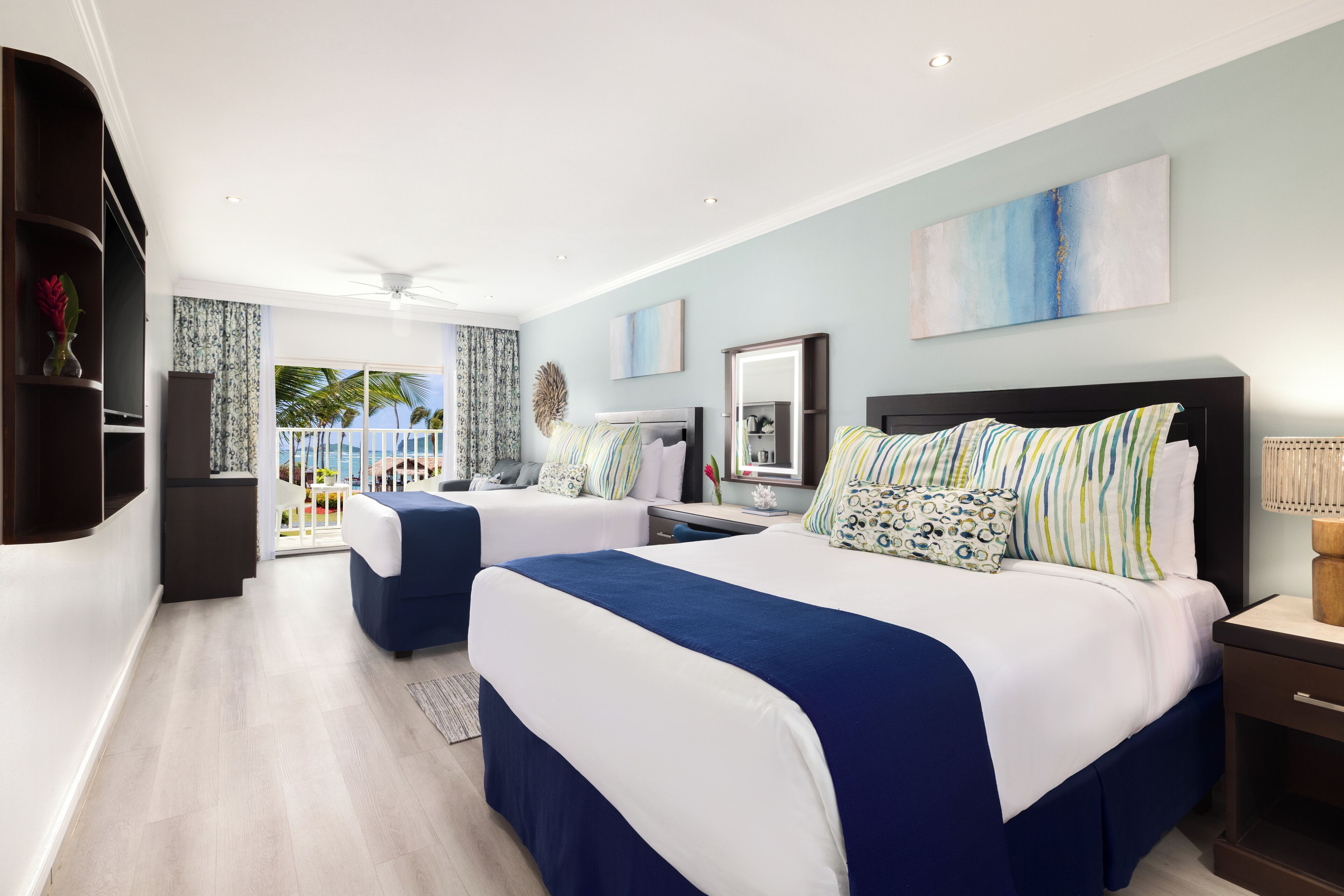 A modern hotel room with two beds, a balcony with a view, and a large painting on the wall.