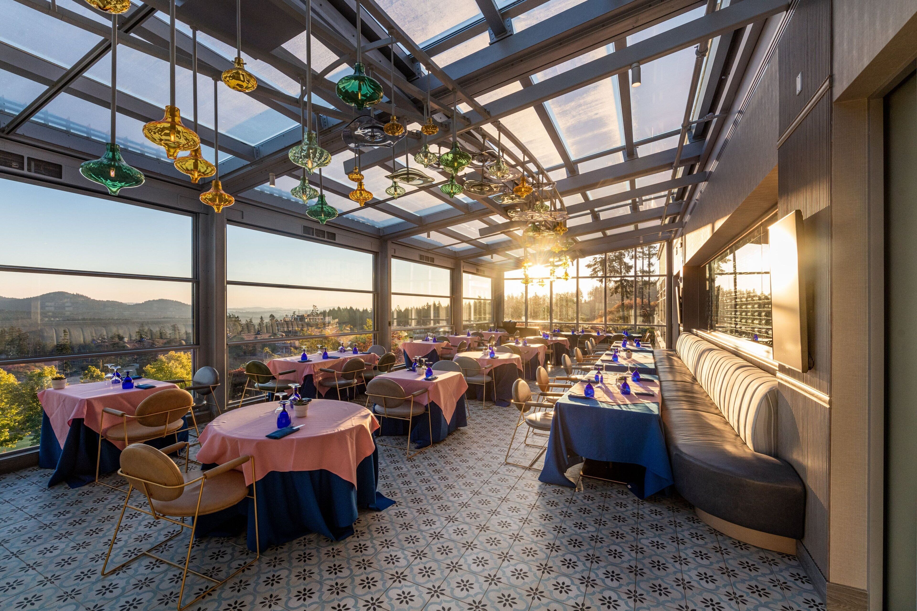 A restaurant with tables set for dining, a bench, and a view of the cityscape.