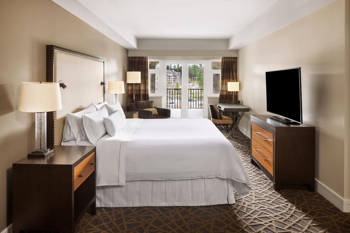 Une chambre d’hôtel avec un grand lit, une télévision, un bureau et un balcon donnant sur l’extérieur.