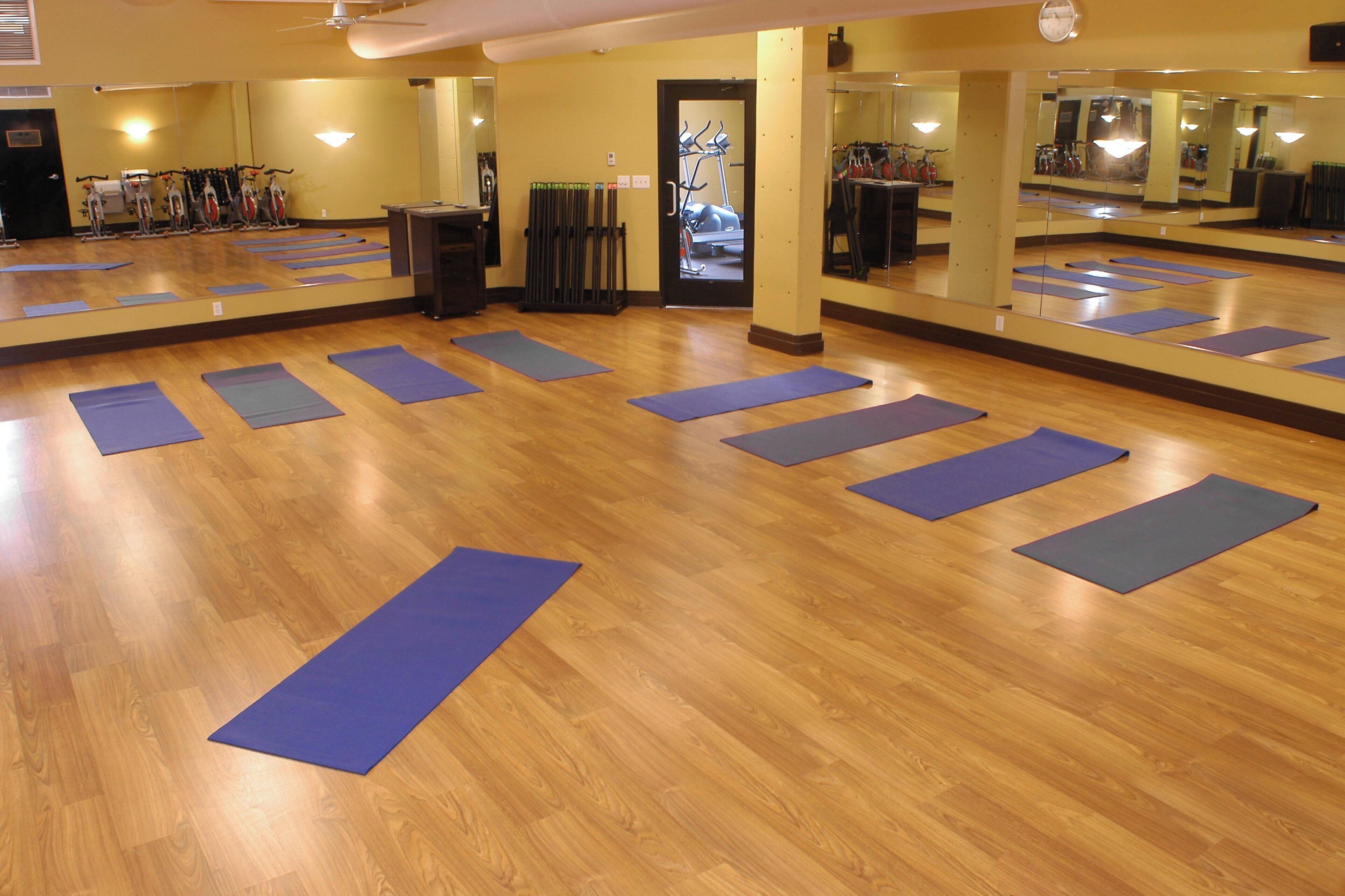 A spacious room with wooden floors and multiple yoga mats arranged for practice.