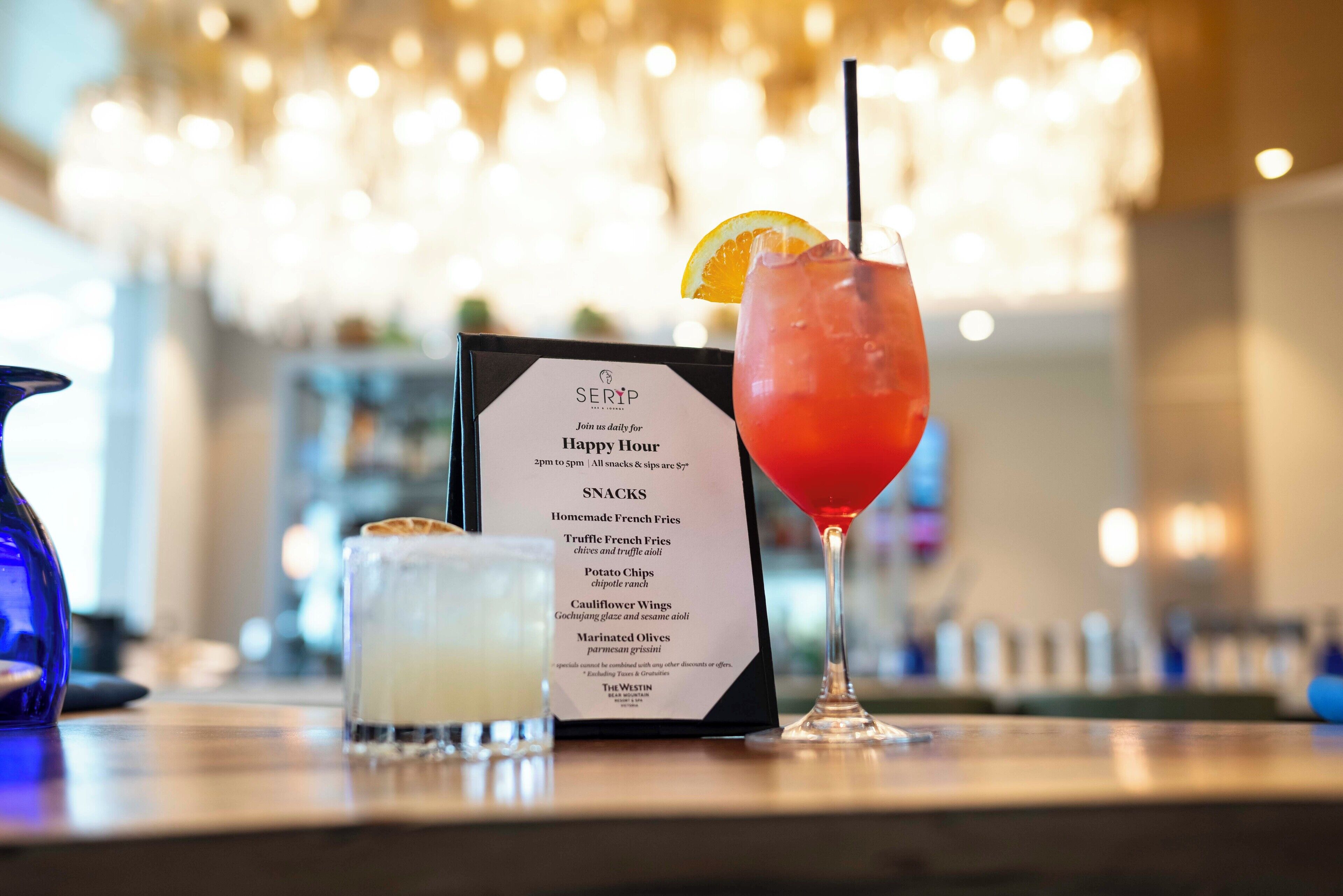 Un bar con una bacheca dei menu, un cocktail rosso guarnito con arancia e un bicchiere di bevanda bianca.