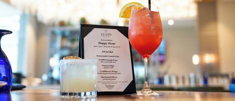 Un bar con una bacheca dei menu, un cocktail rosso guarnito con arancia e un bicchiere di bevanda bianca.