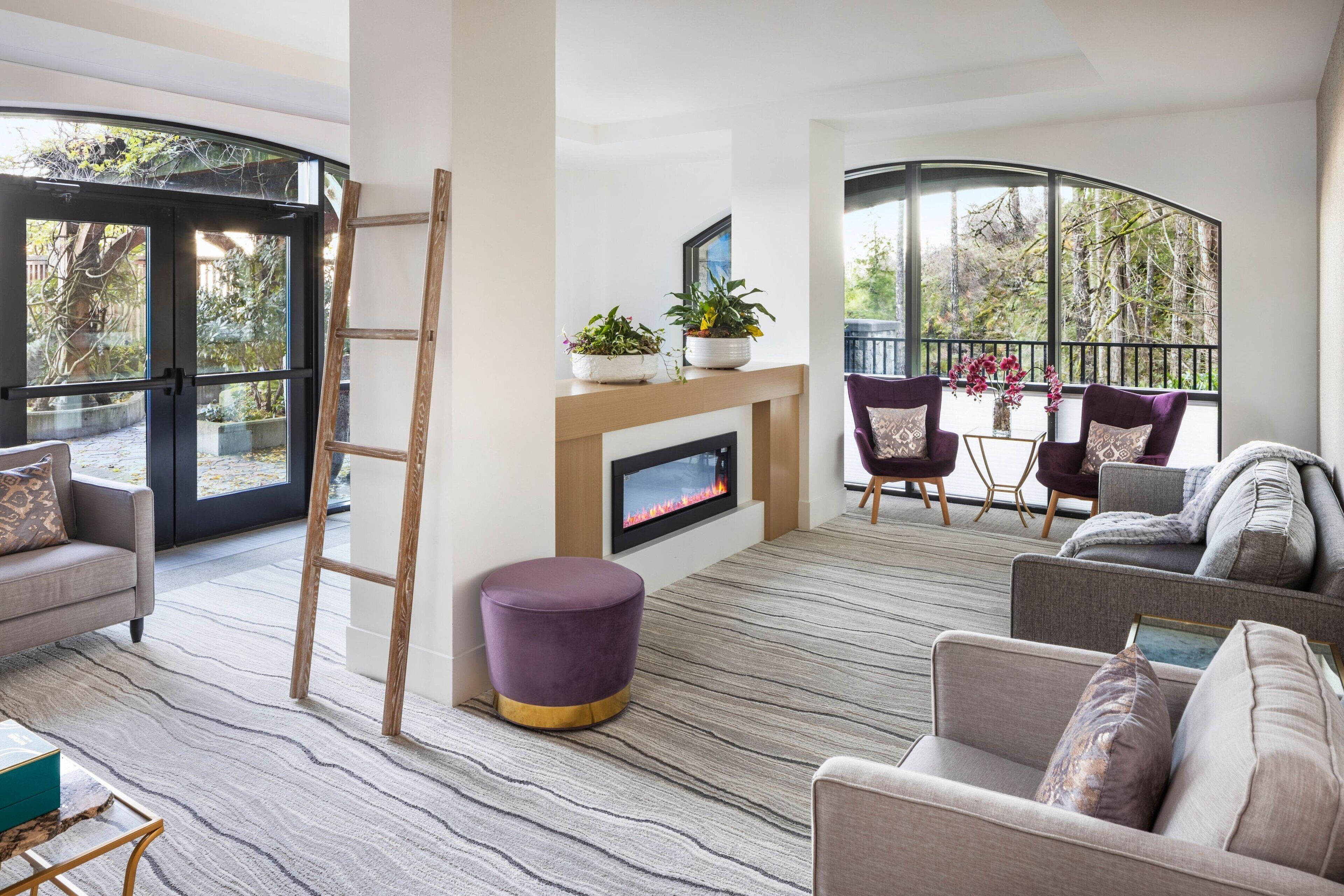 A modern living room with a fireplace, comfortable seating, and large windows offering a view of the outdoors.