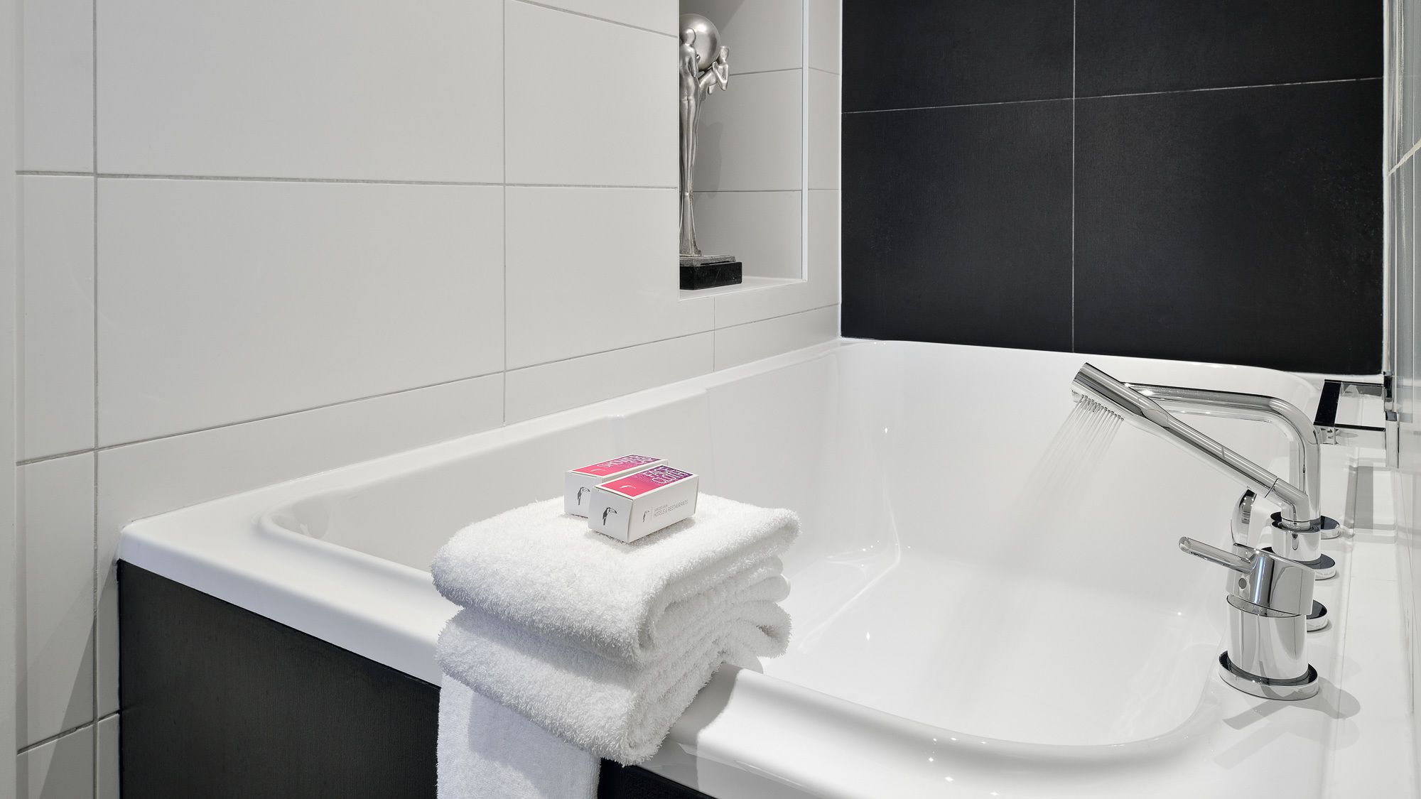 A modern bathroom with a white bathtub, a chrome faucet, and a towel rack with folded towels.