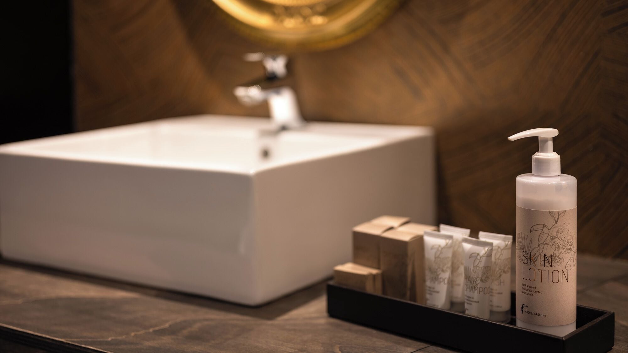 A bathroom with a white sink, a mirror, and a bottle of lotion on a tray.
