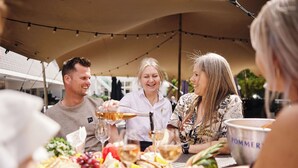 A group of people at a picnic under a tent with a table set with food and drinks.