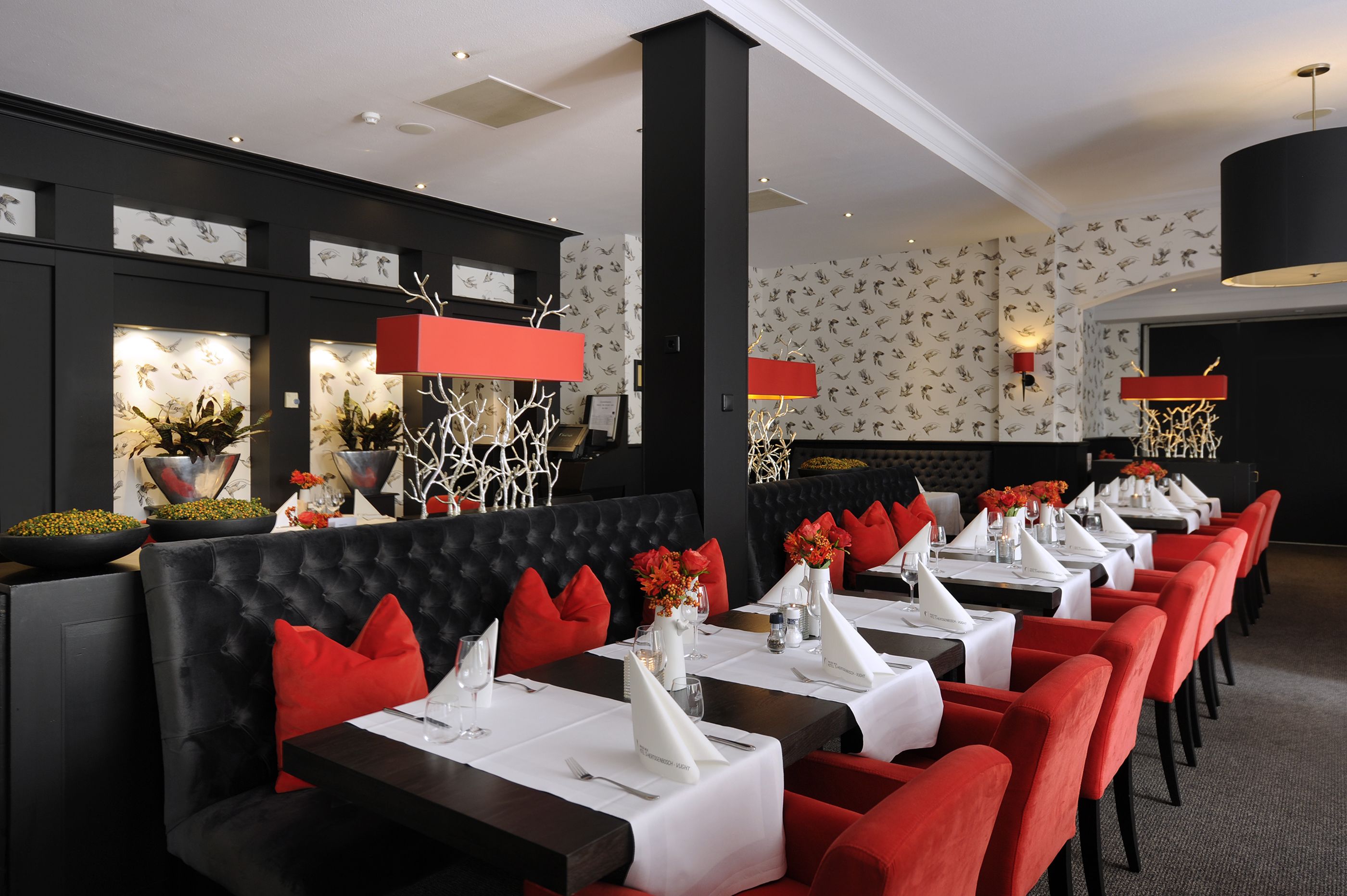 A restaurant with black upholstered booths, red chairs, and white tablecloths.