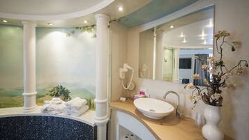 Une salle de bain avec un grand miroir, un lavabo, une baignoire et une plante décorative.