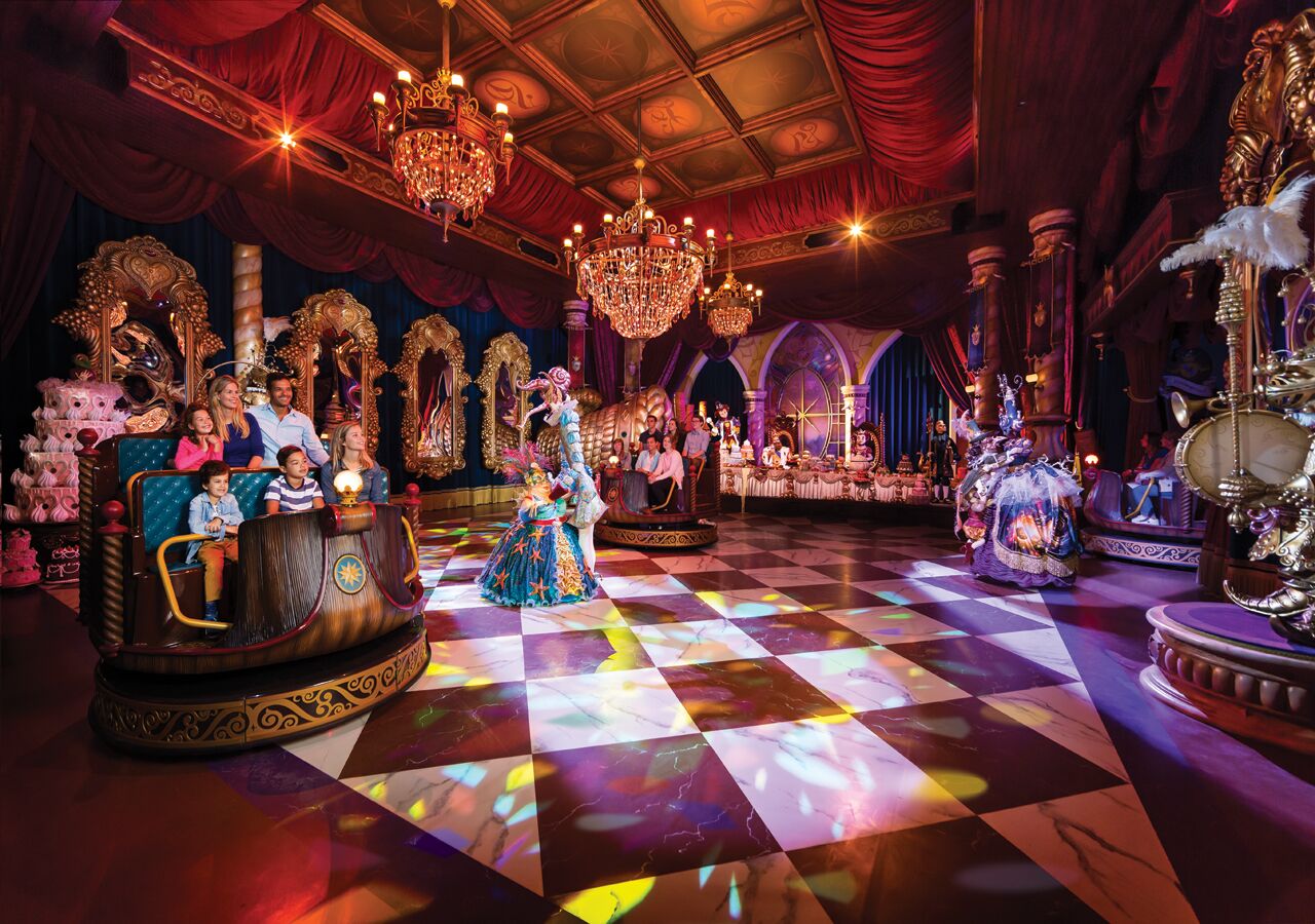 A grand ballroom with ornate chandeliers, a checkered floor, and a stage with performers.